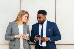 Business people and coworkers talking and using smartphone outside. They wear suits and relax on a break outside the office