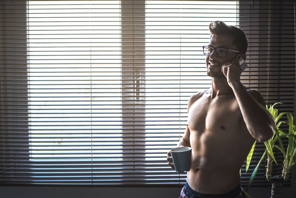 Man standing by a windows blind speaking on the mobile phone