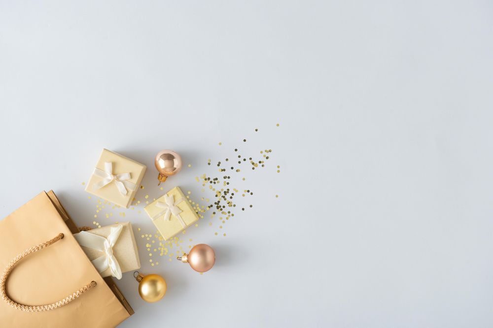 Beige shopping bag on light background with small wrapped presents and glitter