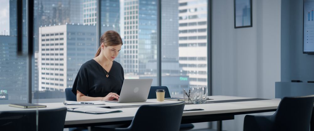 Portrait of Successful Businesswoman Working on Laptop Computer in Her Big City Corner Office.