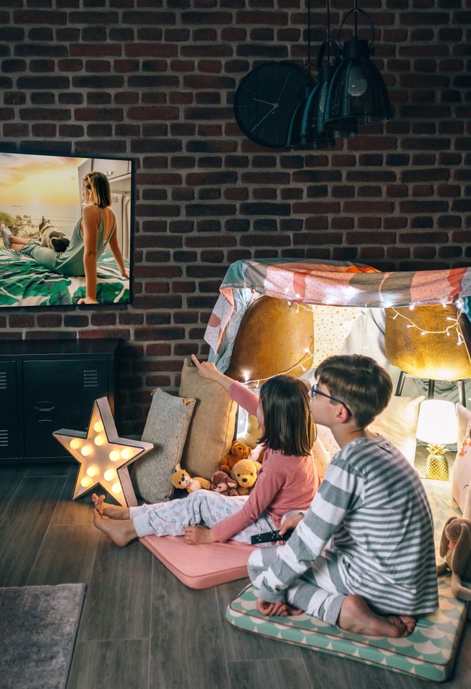 Two concentrated children sitting over mats while watching television program on living room
