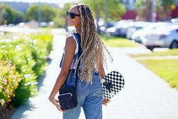Happy female in denim overalls standing with skateboard and looking to her side