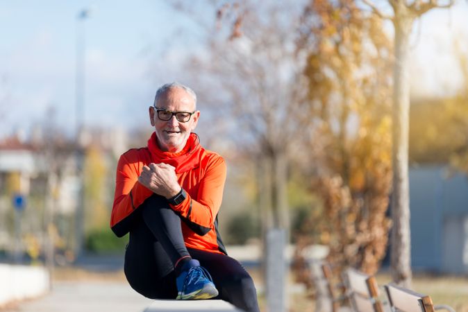 Smiling male sitting on divide in park on autumn day