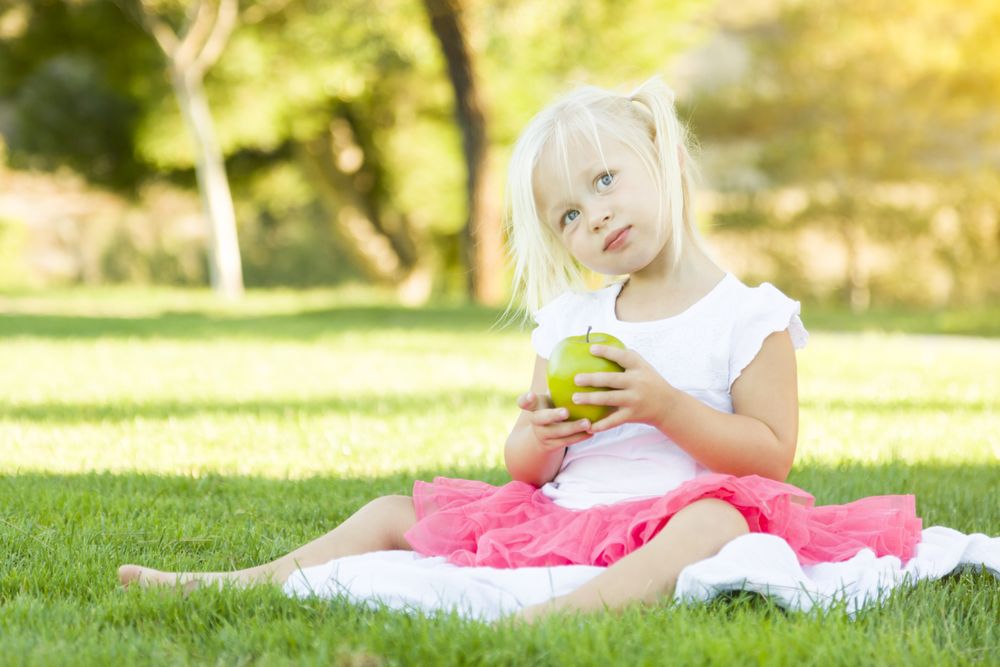 Little Girl In Grass Eating Healthy Apple