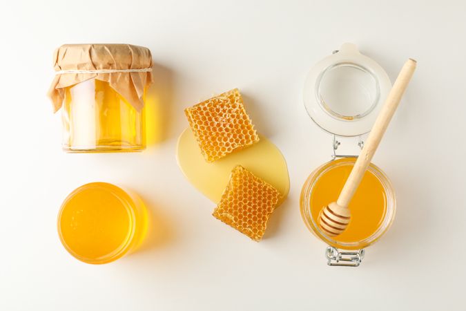 Flat lay. Jars with honey, dipper and honeycomb on neutral background