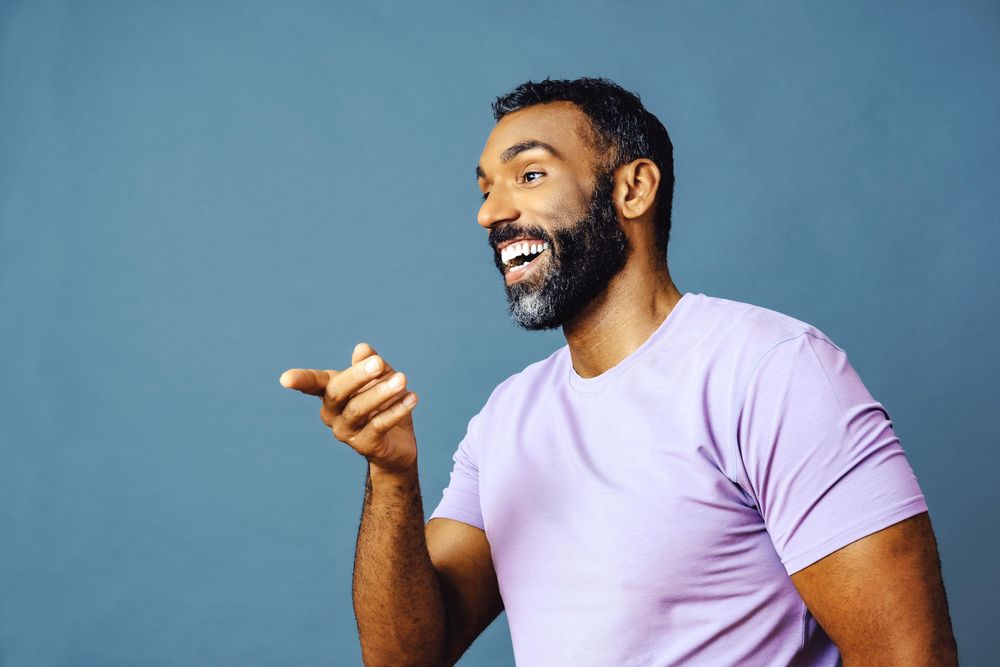 Male talking in purple t-shirt while pointing to the side, copy space
