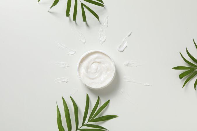 Jar with cream and leaves on light background, top view