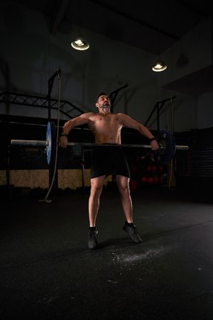 Strong sportsman lifting barbell during training in gym