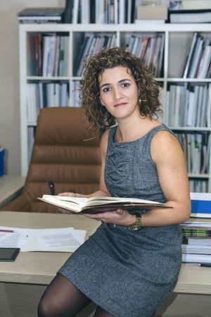 Businesswoman looking up from notebook while sitting on desk