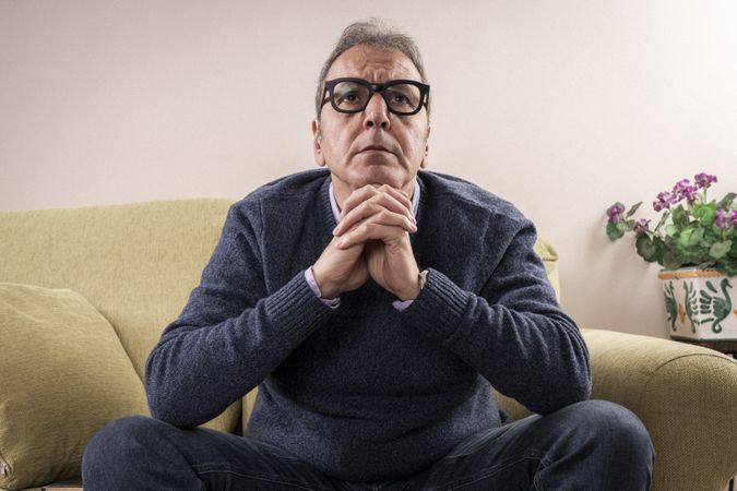 Worried man thinking deeply while sitting on the sofa at home.