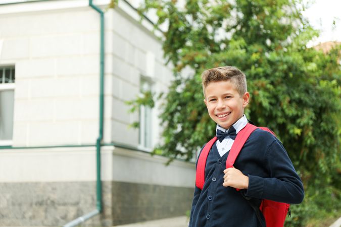Boy with backpack against school building, space for text