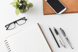 Smartphone, stationary and glasses on table with notebook