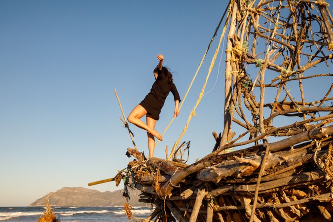 Young woman with upped leg on decorative wooden ship near water on shore