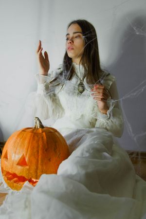 Woman in light dress sitting on floor holding a carved pumpkin