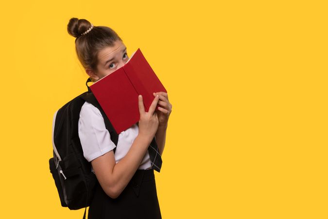 Schoolgirl hides face behind book.