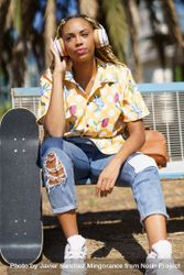 Female in bold patterned shirt sitting on park bench listening to music on large headphones 41Be8b