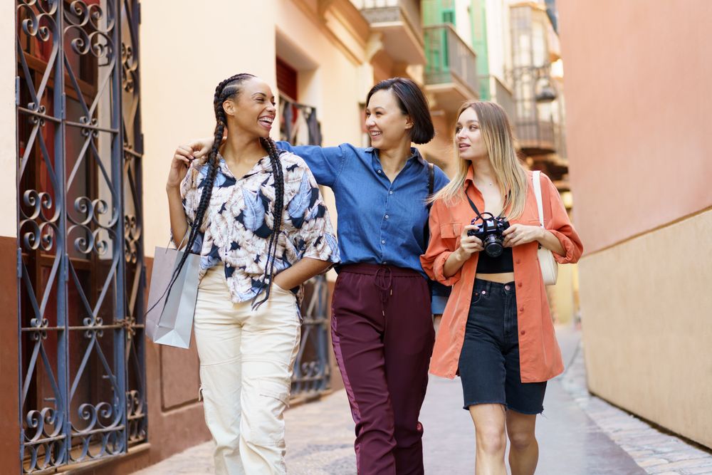 Three laughing women strolling down narrow lane with camera