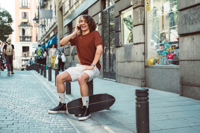 Amused man with longboard talking on phone while resting on street