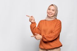 Merry Muslim woman in headscarf and orange sweater pointing to her side with both hands