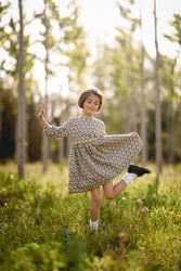 Happy child standing in dress in nature surrounded by trees