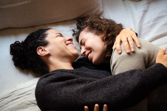 Two women laughing and embracing and lying in bed