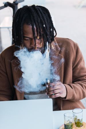 Smoking Black man using laptop on restaurant terrace