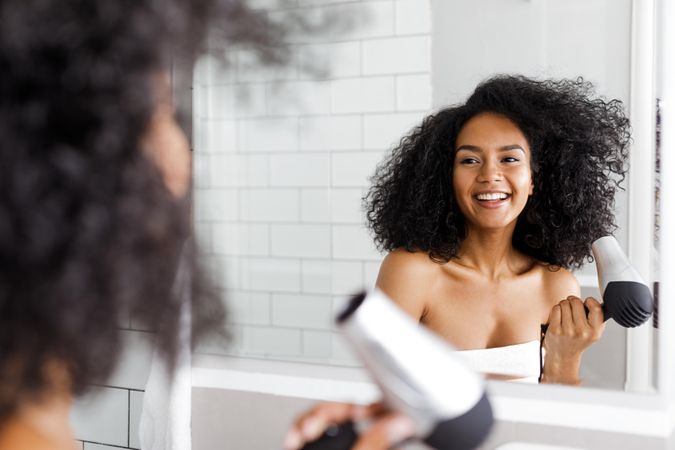 Smiling Black woman styling her hair in light tiled bathroom
