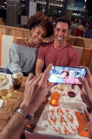 Crop man taking photo of multiethnic couple in bar