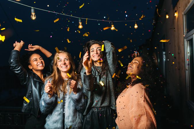 Group of female friends throwing confetti at night
