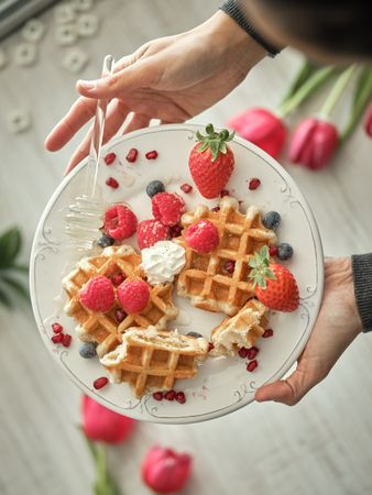 Unrecognizable person pouring honey on waffles