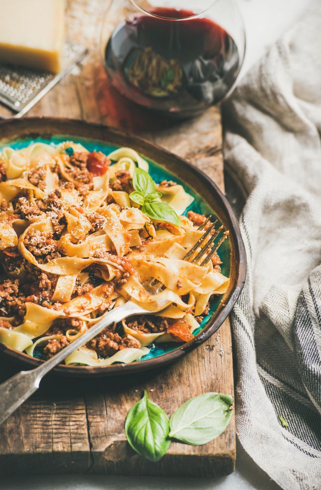 Pasta dinner with minced meat, cheese and red wine on wooden board, close up