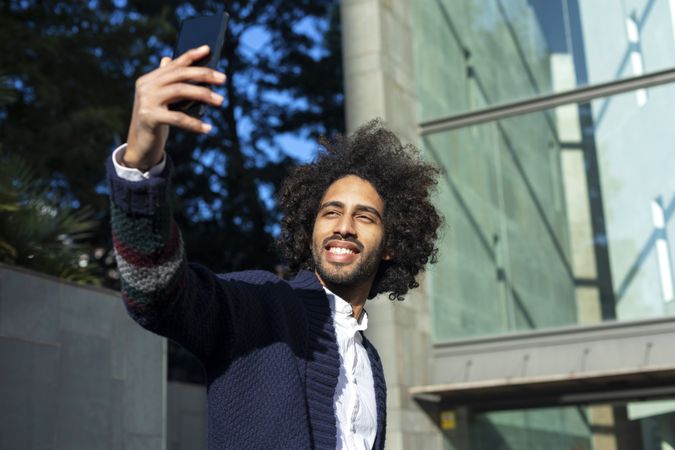 Smiling Black man taking selfie with phone while outside in the sun