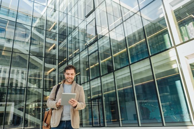 Cheerful businessman using tablet outside office building