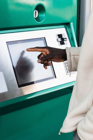 Anonymous Black businessman touching screen of ATM in town