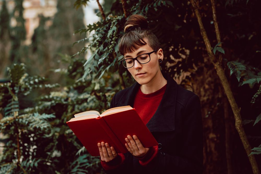 Young woman reading book on bench in park