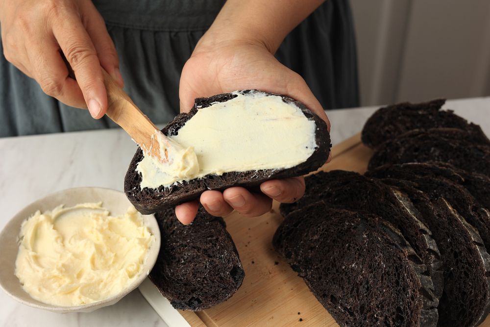 Spreads Cream Cheese with a Wooden Cutlery Knife to the Chocolate Sourdough Bread.