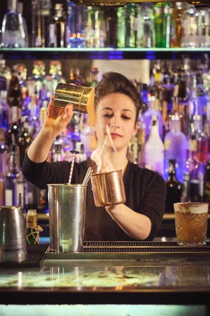 Professional female barkeeper adding salt into flaming cocktail