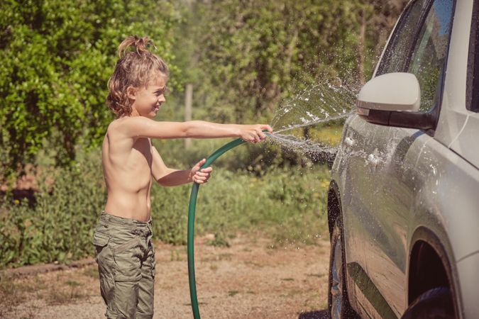 Cheerful boy washing car in countryside