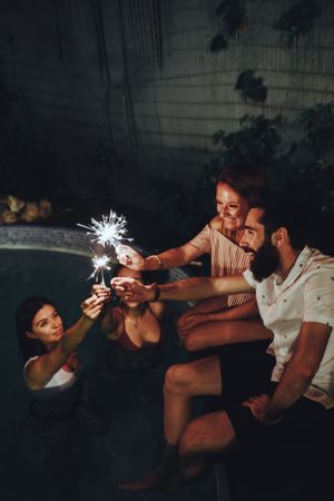 Cheerful friends burning sparkles near pool