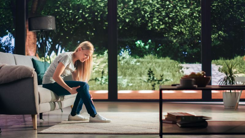 Young Adult Female Had to Sit Down on a Couch at Home Due to Discomfort in a Result of Leg Trauma or Arthritis.