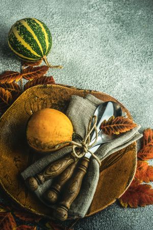 Brown plate in autumnal table setting with gourds and leaves