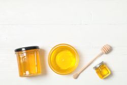 Glass jar and bowl with honey, dipper on wooden background. Flat lay