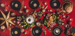 Festive red table setting with cake, roast chicken, stars, bread and decorations