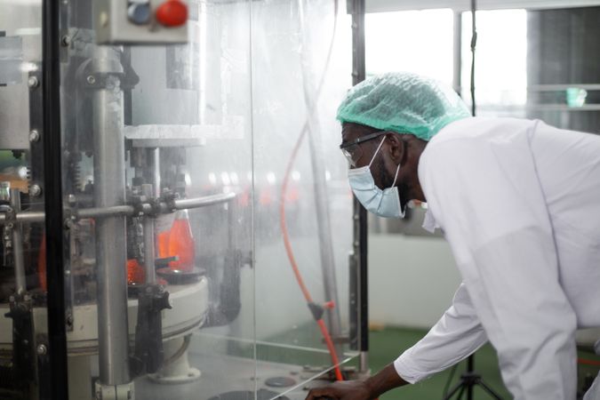 Black male worker inspecting drink product on bottling factory machinery.