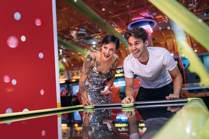 Couple holding strikers and playing air hockey game as a team at a gaming parlour