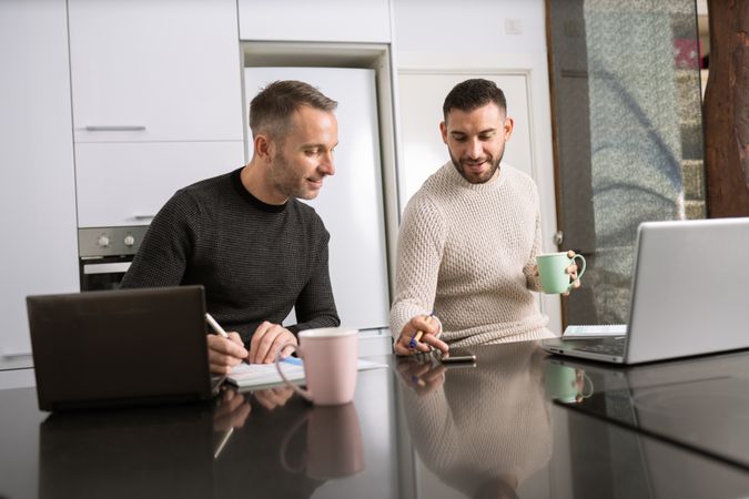 Two men with coffee working from home on kitchen counter