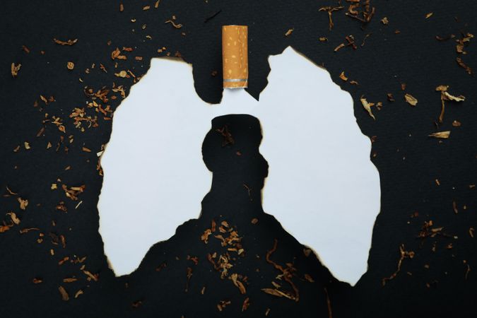 Ripped paper in lung shape with cigarette and tobacco on dark background