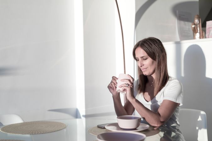 Long haired adult woman sitting at sunny table holding a cup of tea