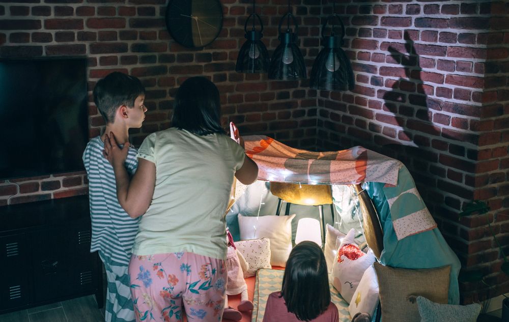 Mother and two children having fun playing with shadow puppets over brick wall at home pajama party