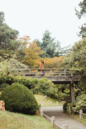 stylish woman leaning on railing of bridge of park in New York looking away